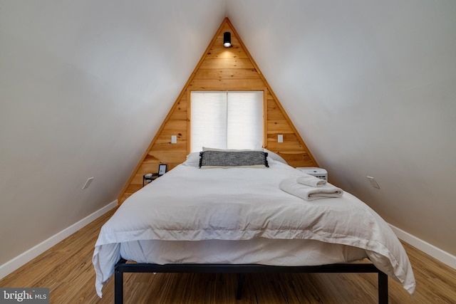 bedroom with hardwood / wood-style floors, wood walls, and vaulted ceiling