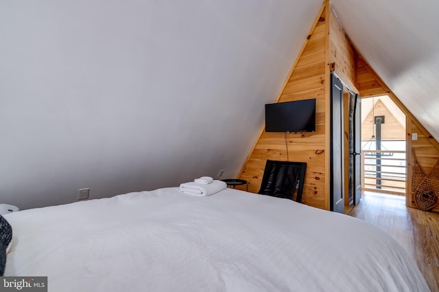 bedroom with wood walls, vaulted ceiling, and hardwood / wood-style flooring