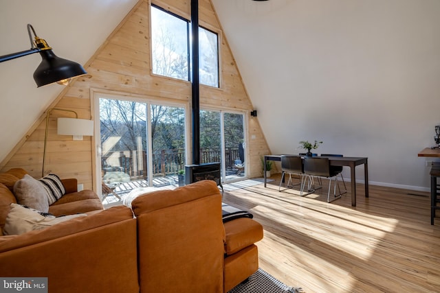 living room with hardwood / wood-style flooring, wood walls, a wood stove, and high vaulted ceiling