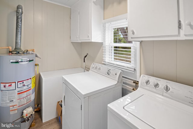 clothes washing area featuring cabinets, washing machine and dryer, water heater, light hardwood / wood-style flooring, and wood walls