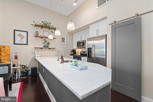 kitchen with dark hardwood / wood-style floors, a barn door, appliances with stainless steel finishes, decorative light fixtures, and kitchen peninsula