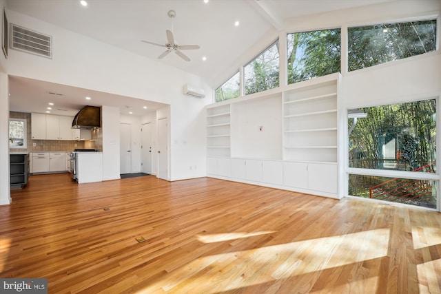 unfurnished living room with light wood-type flooring, a wall unit AC, ceiling fan, beam ceiling, and high vaulted ceiling