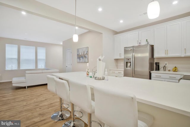 kitchen featuring a kitchen breakfast bar, light wood-type flooring, decorative light fixtures, white cabinets, and stainless steel fridge with ice dispenser