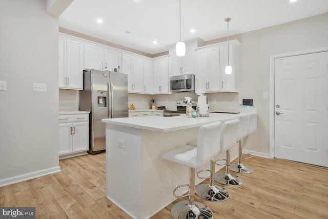 kitchen with pendant lighting, white cabinets, stainless steel appliances, and light hardwood / wood-style floors