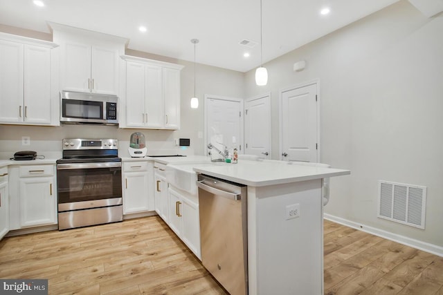 kitchen with white cabinets, appliances with stainless steel finishes, light hardwood / wood-style floors, and pendant lighting