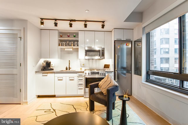 kitchen with appliances with stainless steel finishes, backsplash, sink, white cabinets, and light hardwood / wood-style floors