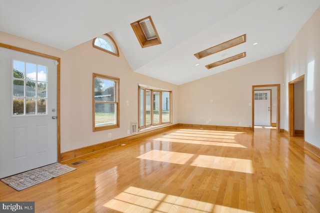 interior space with light wood-type flooring, a skylight, and high vaulted ceiling