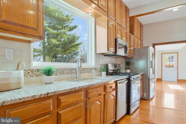 kitchen with light stone countertops, appliances with stainless steel finishes, tasteful backsplash, sink, and light wood-type flooring