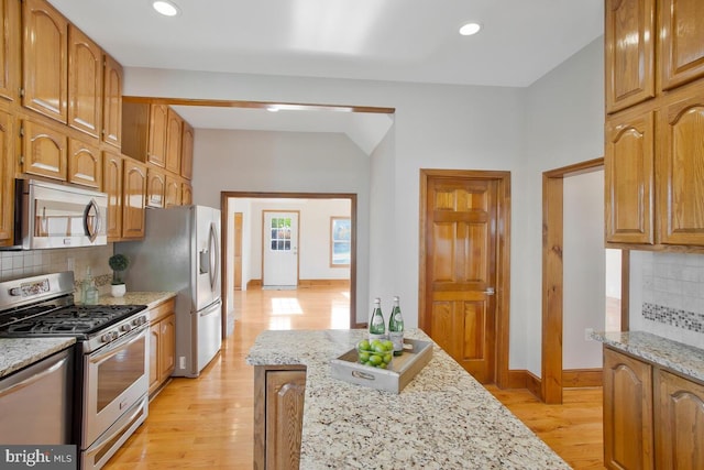 kitchen featuring decorative backsplash, light stone countertops, appliances with stainless steel finishes, and light hardwood / wood-style flooring