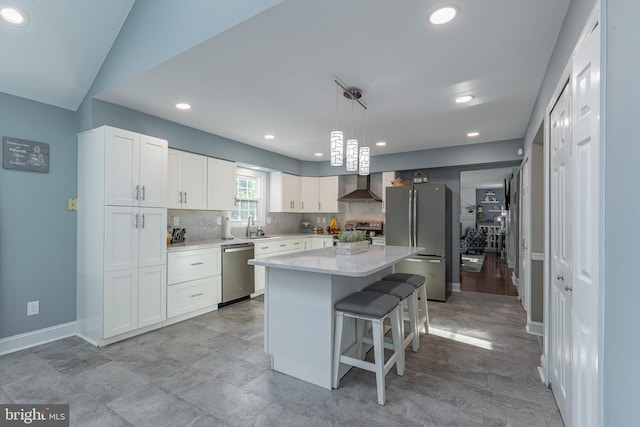 kitchen with a center island, white cabinets, wall chimney range hood, appliances with stainless steel finishes, and decorative light fixtures