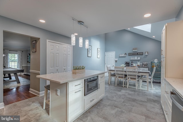 kitchen featuring appliances with stainless steel finishes, light wood-type flooring, white cabinets, a kitchen island, and hanging light fixtures