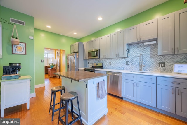 kitchen featuring sink, a kitchen island, appliances with stainless steel finishes, light hardwood / wood-style floors, and a breakfast bar area