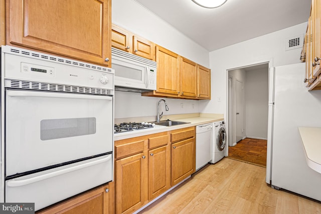 kitchen with washer / dryer, white appliances, light hardwood / wood-style flooring, and sink