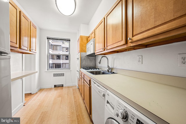 kitchen with white appliances, radiator, sink, washer and dryer, and light hardwood / wood-style floors