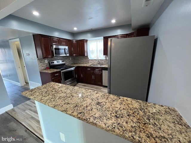 kitchen featuring light stone countertops, appliances with stainless steel finishes, decorative backsplash, sink, and light hardwood / wood-style flooring