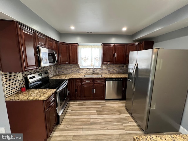 kitchen with light stone countertops, backsplash, stainless steel appliances, sink, and light hardwood / wood-style floors