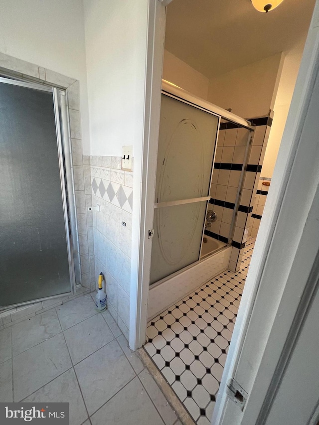 bathroom with tile patterned floors, bath / shower combo with glass door, and tile walls