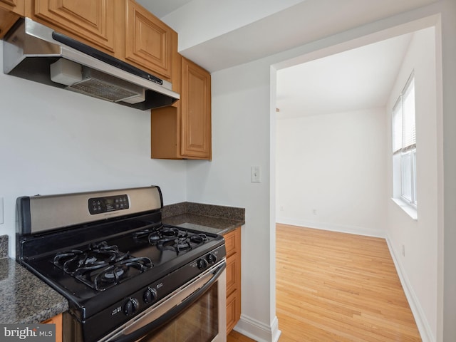 kitchen with gas stove, light hardwood / wood-style flooring, and dark stone countertops