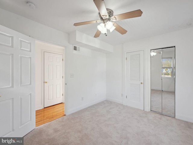 unfurnished bedroom with light carpet, ceiling fan, and two closets