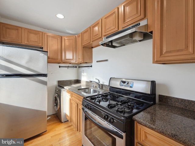 kitchen with sink, light hardwood / wood-style flooring, dark stone countertops, appliances with stainless steel finishes, and washer / dryer