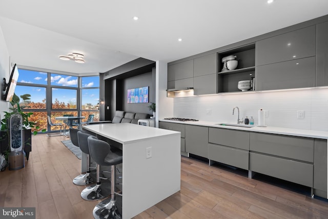 kitchen with gray cabinetry, sink, a wall of windows, a center island, and a breakfast bar area