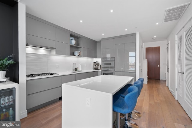 kitchen with a kitchen bar, gray cabinetry, sink, a kitchen island, and stainless steel gas stovetop