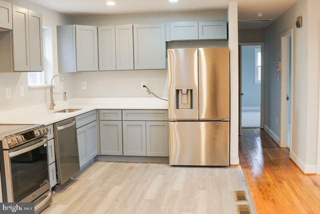 kitchen with gray cabinetry, light hardwood / wood-style floors, sink, and appliances with stainless steel finishes