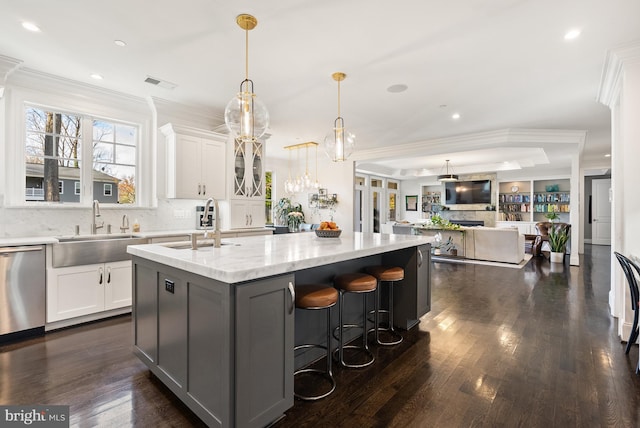 kitchen with a tray ceiling, stainless steel dishwasher, white cabinets, and a center island with sink