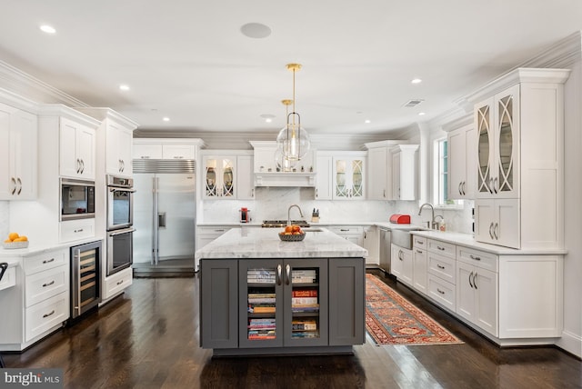 kitchen with pendant lighting, beverage cooler, a center island, white cabinetry, and built in appliances