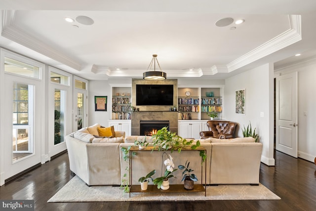 living room featuring built in shelves, a fireplace, dark hardwood / wood-style floors, a tray ceiling, and crown molding