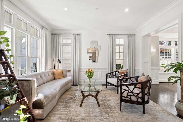 living area with a wealth of natural light, ornamental molding, and hardwood / wood-style flooring