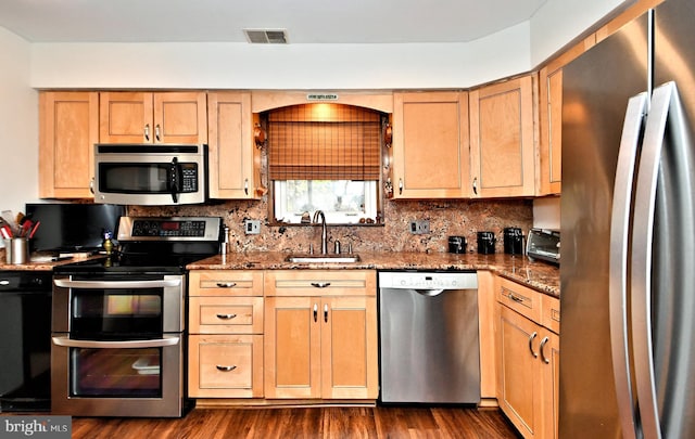 kitchen with decorative backsplash, appliances with stainless steel finishes, dark stone counters, sink, and dark hardwood / wood-style floors