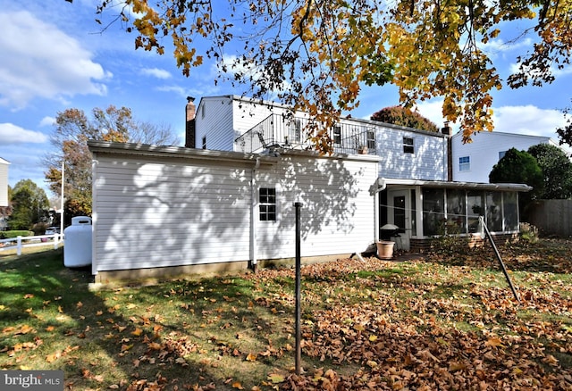 rear view of house with a balcony, a lawn, and a sunroom