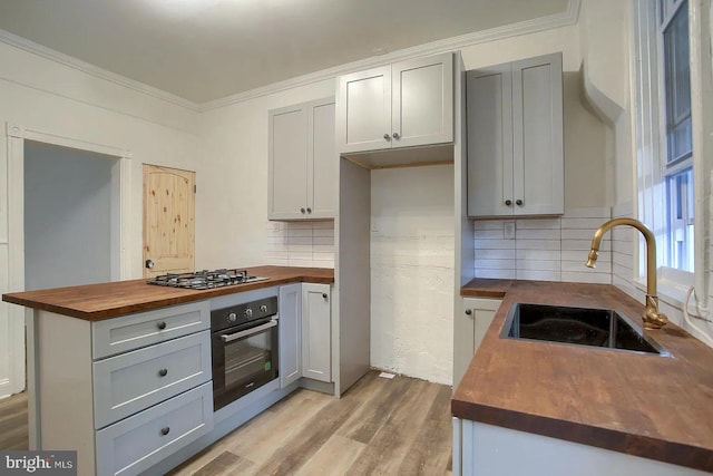 kitchen featuring sink, light wood-type flooring, appliances with stainless steel finishes, tasteful backsplash, and butcher block counters