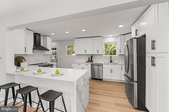 kitchen with white cabinetry, wall chimney exhaust hood, kitchen peninsula, plenty of natural light, and appliances with stainless steel finishes