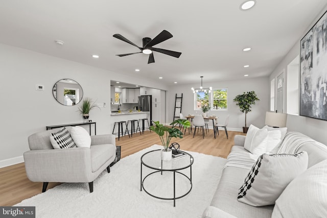 living room with ceiling fan with notable chandelier and light hardwood / wood-style flooring