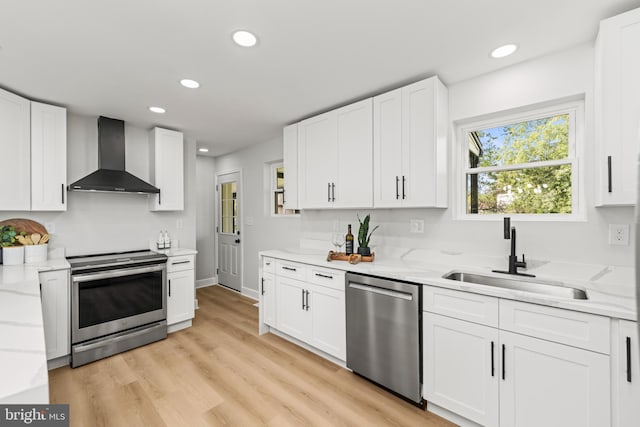 kitchen featuring appliances with stainless steel finishes, sink, wall chimney range hood, light hardwood / wood-style flooring, and white cabinetry