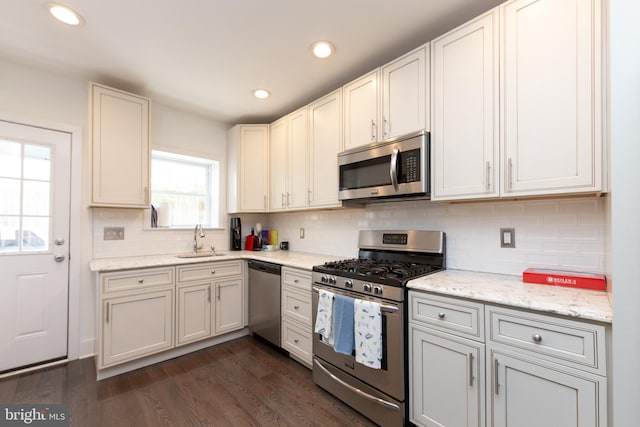 kitchen with light stone countertops, appliances with stainless steel finishes, dark hardwood / wood-style flooring, sink, and white cabinetry