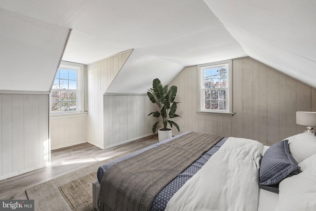 bedroom featuring wooden walls, vaulted ceiling, and light wood-type flooring