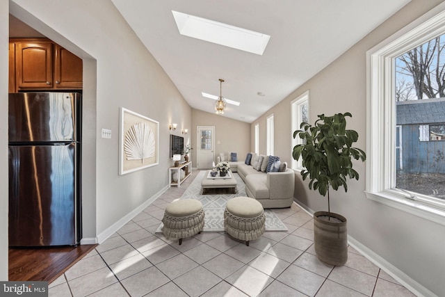 living room featuring ceiling fan, vaulted ceiling with skylight, and light tile patterned floors