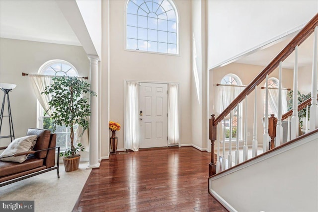 entrance foyer featuring a towering ceiling, dark hardwood / wood-style flooring, and decorative columns