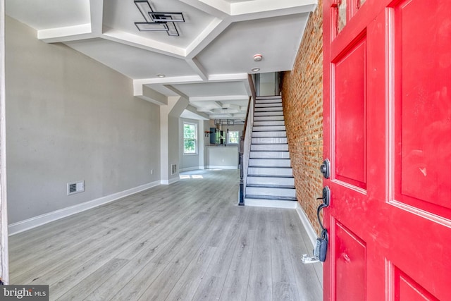 entrance foyer featuring beamed ceiling, brick wall, and light wood-type flooring