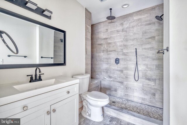 bathroom featuring hardwood / wood-style flooring, vanity, toilet, and tiled shower