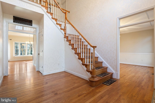 stairway featuring crown molding, wood-type flooring, and a notable chandelier