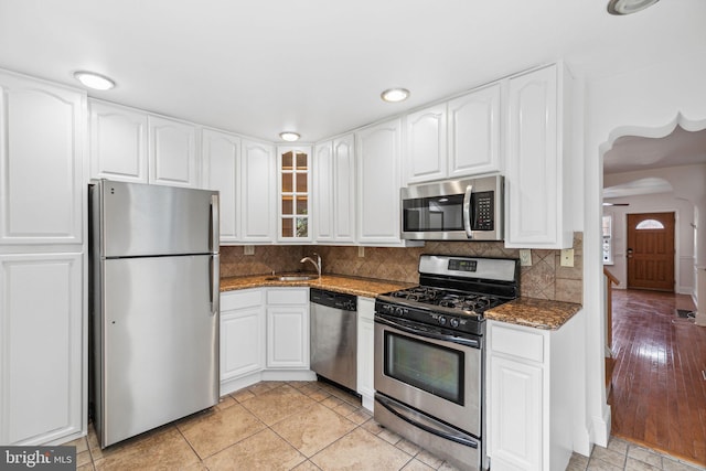 kitchen featuring dark stone counters, white cabinets, sink, light wood-type flooring, and appliances with stainless steel finishes