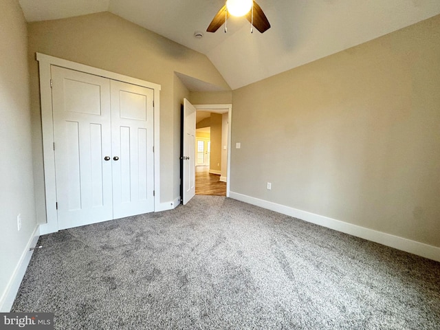 unfurnished bedroom featuring lofted ceiling, a closet, carpet flooring, and baseboards