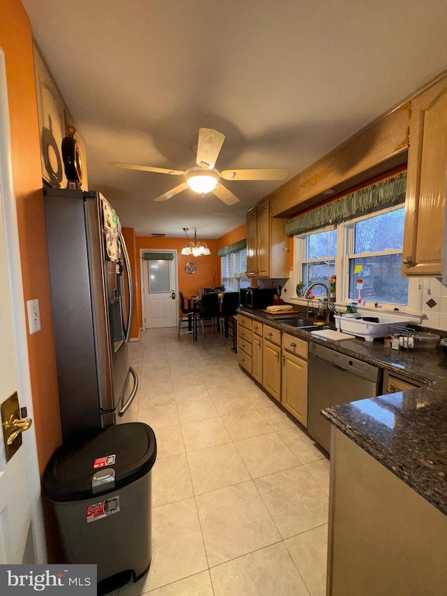 kitchen featuring ceiling fan with notable chandelier, sink, dark stone countertops, light tile patterned floors, and appliances with stainless steel finishes