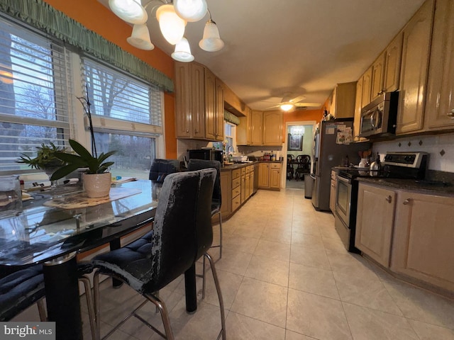 kitchen featuring pendant lighting, ceiling fan with notable chandelier, sink, light tile patterned flooring, and stainless steel appliances