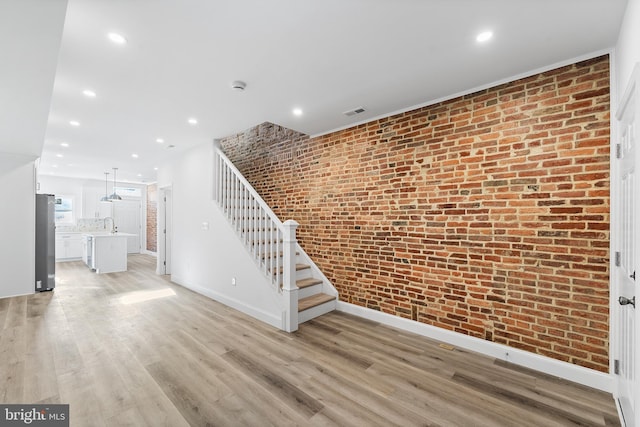 unfurnished living room featuring light wood-type flooring, sink, and brick wall