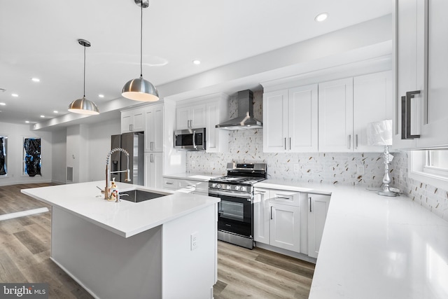 kitchen with a kitchen island with sink, white cabinets, wall chimney range hood, and appliances with stainless steel finishes